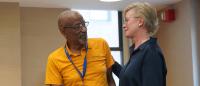 Robert Fullilove and Kathleen Sikkema stand in a classroom; they look at each other and smile
